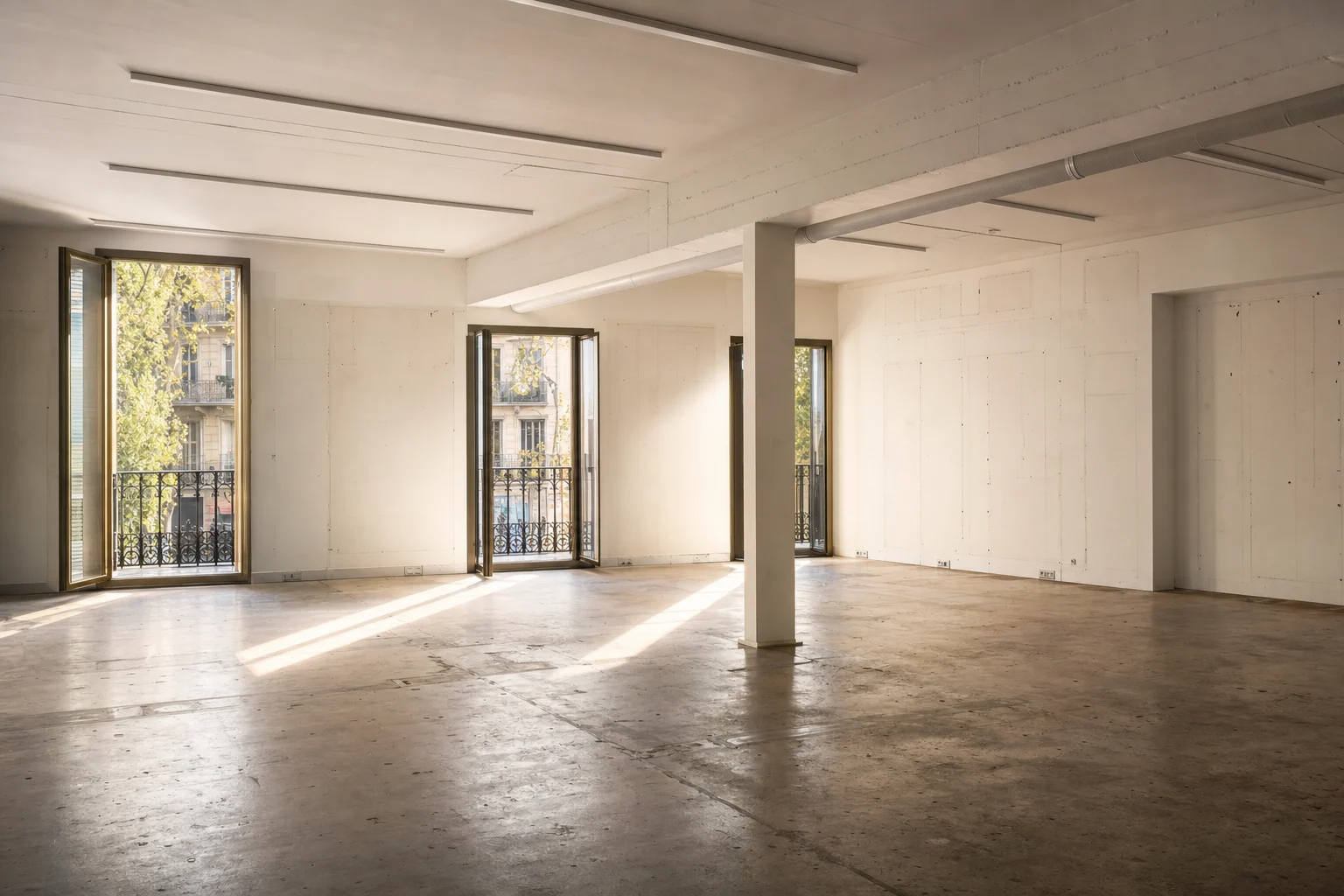 Local diáfano de Barcelona completamente vacío tras el desmantelamiento, con las puertas de balcón abiertas a la luz de la tarde y el suelo barrido