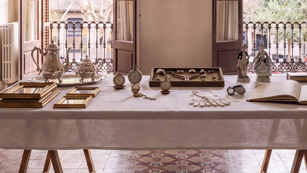 Mesa de caballetes con un servicio de plata, relojes de bolsillo, una bandeja de joyas, guantes blancos y un libro de registro abierto