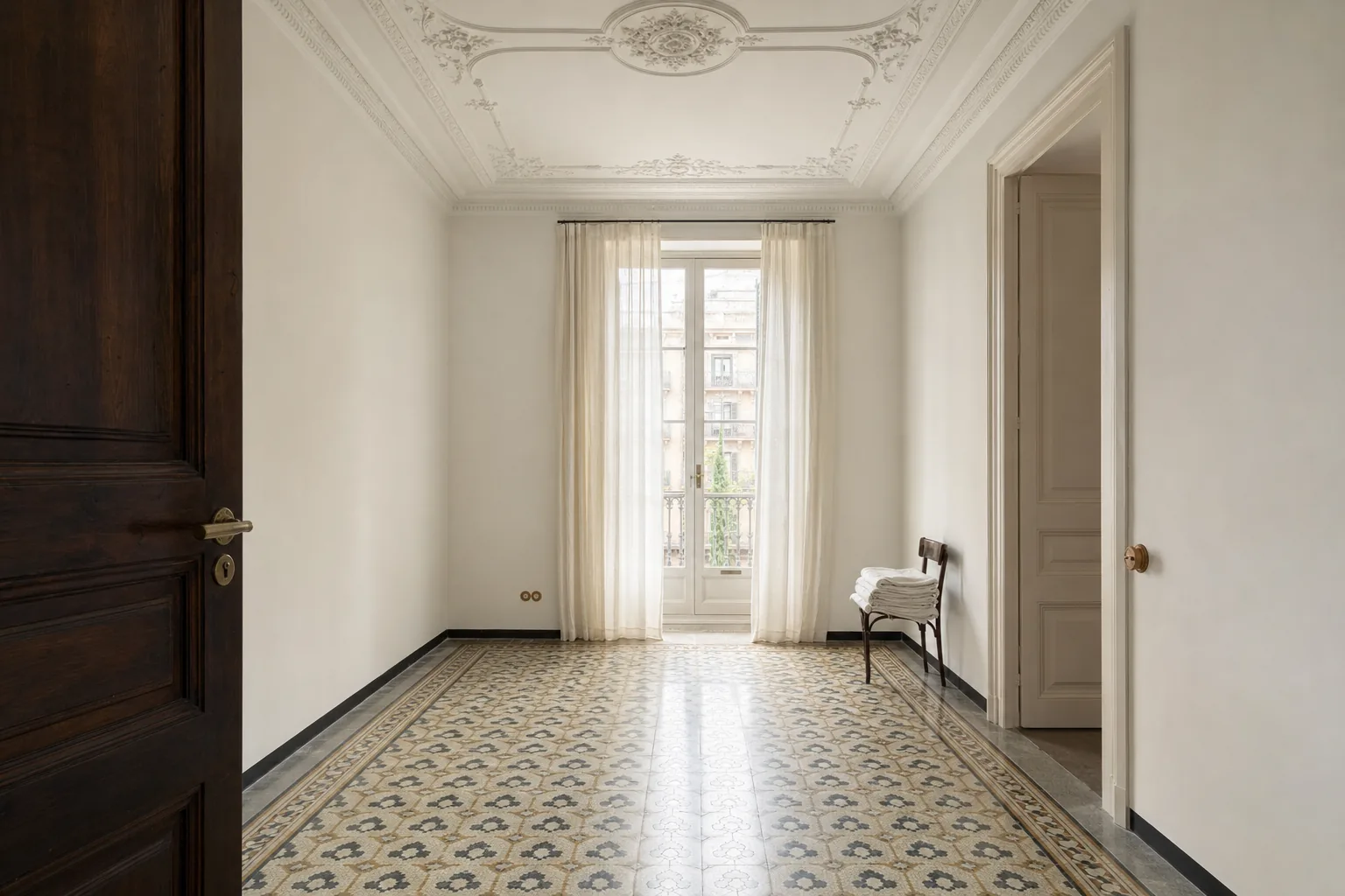 Dormitorio vacío de un piso del Eixample con visillos que filtran la luz y paños blancos doblados sobre una silla