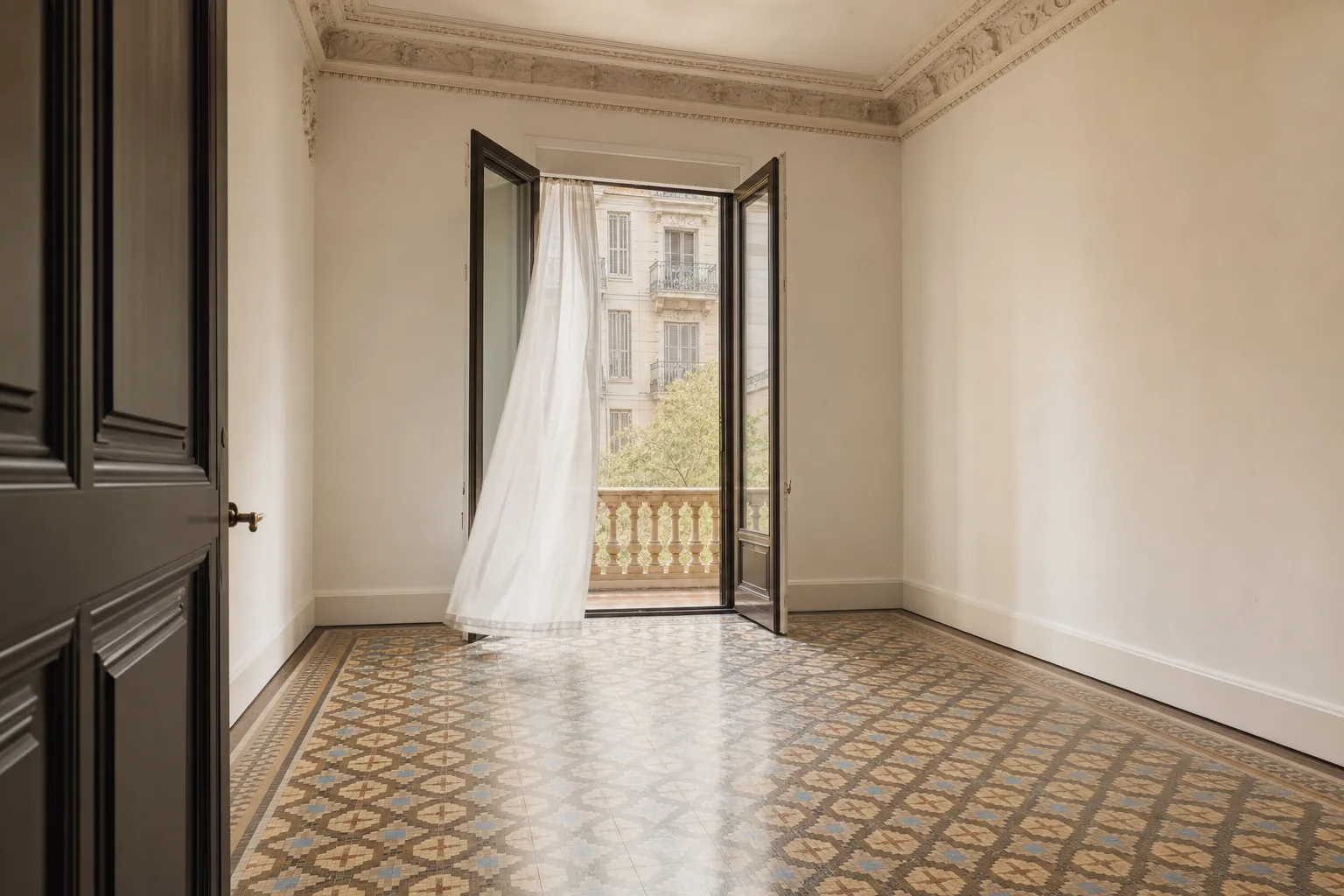 Dormitorio del Eixample limpio y aireado, vacío, con el visillo moviéndose en la puerta del balcón abierta a la luz de la mañana